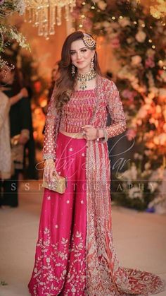 a woman in a pink lehenga and gold jewelry standing under a chandelier