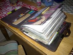 a wooden table topped with lots of books and papers on top of it next to a chair