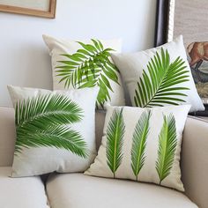 three pillows with palm leaves on them sit on a couch in front of a painting