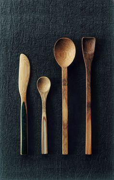 four wooden spoons and two green wood spoons on a black surface with dark background