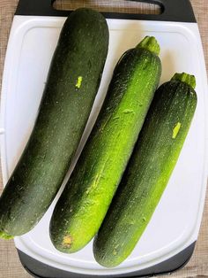 three green cucumbers sitting on top of a cutting board