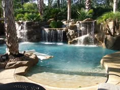 an outdoor pool with waterfall and lounge chairs in the foreground, surrounded by palm trees