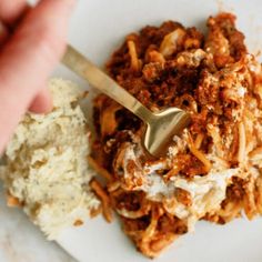 a person is holding a spoon over some food on a plate with rice and meat