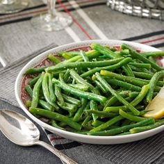 a bowl filled with green beans and lemon wedges on top of a place mat