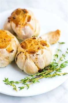 three garlics on a plate with some sprig of thyerole next to them