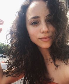 a close up of a person with curly hair and an orange top holding a cell phone