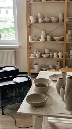 a table topped with lots of white bowls and cups on top of wooden shelves next to a window