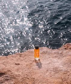 an orange bottle sitting on top of a sandy beach next to the ocean with water splashing in the background