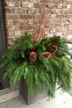 a potted plant with pine cones and greenery in front of a brick wall