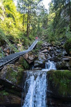 a waterfall with steps leading up to it and people walking on the bridge over it