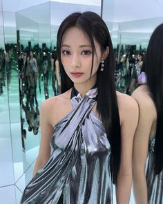 a woman with long black hair standing in front of a mirror wearing a silver dress