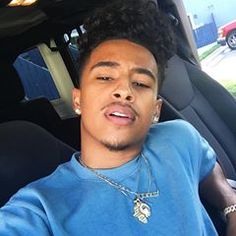 a young man sitting in the back seat of a car wearing a blue shirt and silver necklace