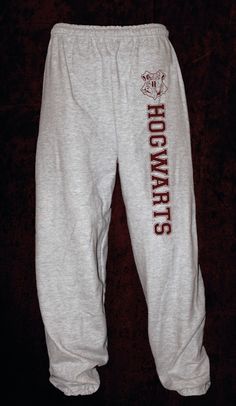 a pair of sweatpants with hogwarts printed on the bottom and side, sitting against a dark background