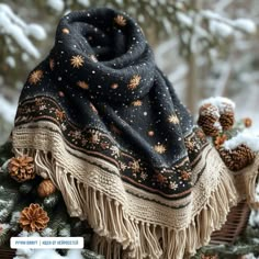 a black and white blanket sitting on top of a tree covered in snow next to pine cones