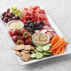 a platter filled with fruit, vegetables and crackers on a marble counter top