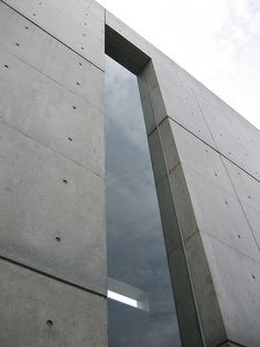 an open window in the side of a concrete building with sky and clouds behind it