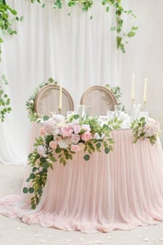 the table is covered with pink chiffon and has candles on it, surrounded by greenery