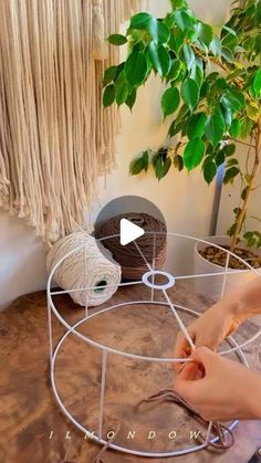 a woman is working with yarn on a table next to a potted plant and knitting needles