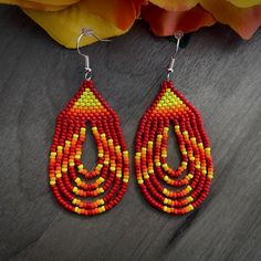 a pair of red, yellow and orange beaded earrings on top of a wooden table