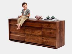 a young boy sitting on top of a wooden dresser