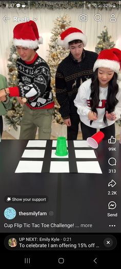 three people standing around a table with christmas decorations on it and one person wearing a santa hat