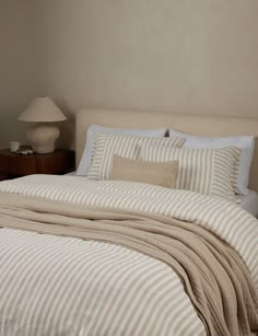 a bed with striped sheets and pillows in a small room next to a night stand