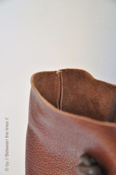 a brown leather bag is sitting on a table next to a white wall and the bottom part of the bag has a hole in it