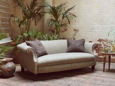 a couch sitting next to a potted plant on top of a brick floor in front of a white brick wall