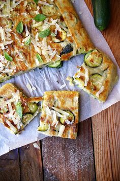 a pizza with zucchini, cheese and other toppings sitting on top of a piece of parchment paper