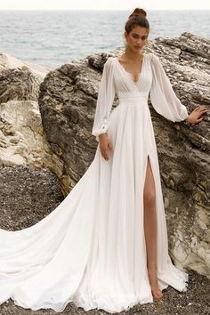 a woman in a white dress standing on rocks near the ocean