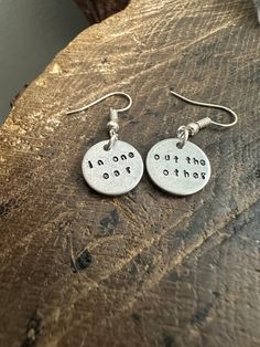 two silver earrings with words on them sitting on top of a piece of wood