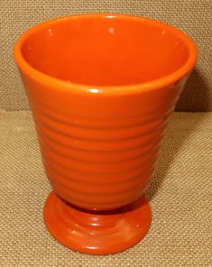 an orange cup sitting on top of a brown cloth covered table next to a wall