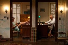 two people sitting at a desk in an old fashioned room with paintings on the walls