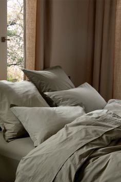 an unmade bed with many pillows in front of a window