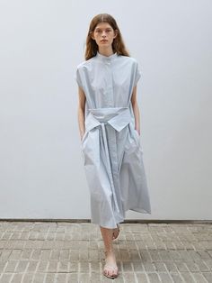 This is WHEN WE WILL’s belted long shirt dress. This is made from a high-density cotton blend fabric. It features an oversized fit with dropped shoulders that create cap sleeves, a high neck collar, and a hidden placket for a clean silhouette. The dress has a relaxed fit and long length, allowing it to be worn open as an outer layer. It includes functional pockets on both sides and uses side slits at the waist to insert the matching fabric belt, allowing for versatile styling without the need for belt loops. This essential item can be styled in various silhouettes depending on how the belt is worn.- Perfect for daily wear- Can be paired with different styles of accessorize to create various looks- The clean design makes it easy to style with any outfit High Neck Collar, Long Shirt Dress, Fabric Belt, Long Shirt, Clean Design, Neck Collar, Long Length, Different Styles, Jumpsuit Dress