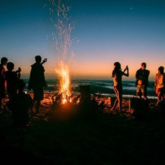 people standing around a campfire at the beach