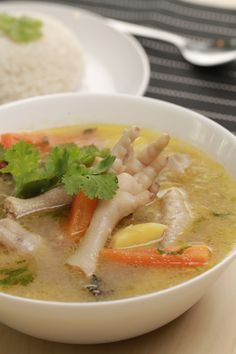 a white bowl filled with soup next to a plate of rice and carrots on a table