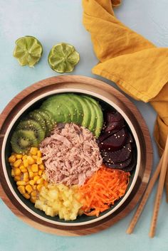 a wooden bowl filled with different types of food next to chopsticks and a yellow napkin