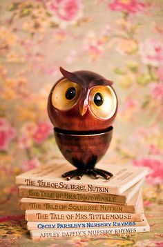 an owl figurine sitting on top of three books in front of a floral background