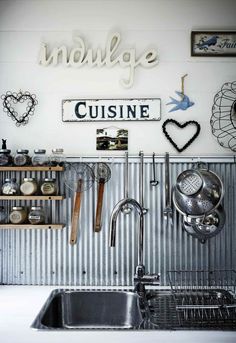 there is a metal sink and shelves in the kitchen with utensils hanging on the wall