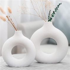 two white vases with plants in them sitting on a table next to a couch