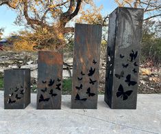 three metal sculptures sitting on top of a cement ground next to a tree and bushes