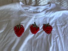 three embroidered strawberries on a white t - shirt with red stitching around the edges