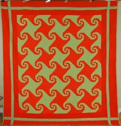 an orange and green quilt hanging on a wall