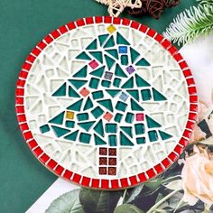 a mosaic christmas tree ornament sitting on top of a table next to flowers