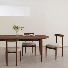 a wooden table with two chairs and a book on it, in front of a white wall