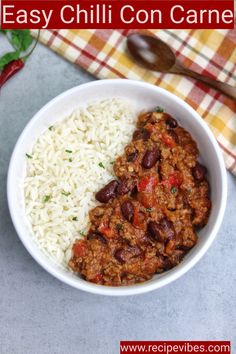 a white bowl filled with rice and chili next to a spoon on a checkered table cloth