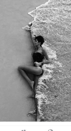 a woman in a bathing suit laying on the beach next to the ocean with her head down