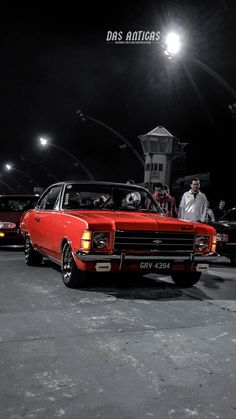 an old red car parked in a parking lot at night