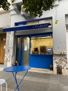 a blue table sitting in front of a building next to a tree and sidewalk with newspaper on it